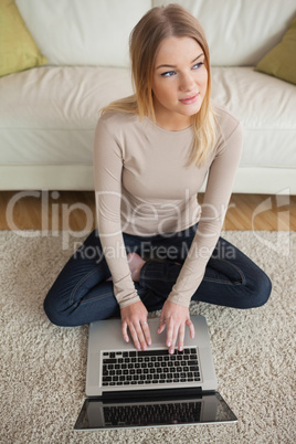 Thoughtful woman sitting on floor using laptop