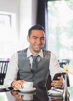 Smiling businessman having coffee and holding phone