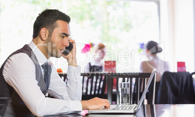 Serious businessman man calling on phone using laptop