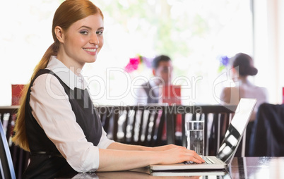 Smiling businesswoman working on laptop looking at camera
