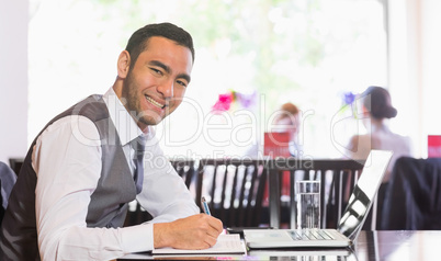 Smiling businessman writing while looking at camera