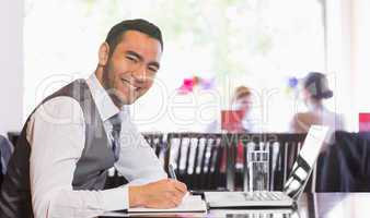 Smiling businessman writing while looking at camera