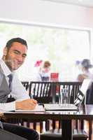 Happy businessman writing while smiling at camera