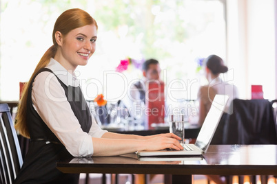 Happy businesswoman typing on laptop while smiling at camera