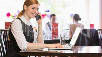 Smiling businesswoman calling on phone typing on laptop and look