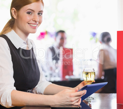 Attractive businesswoman holding tablet and wine glass and smili