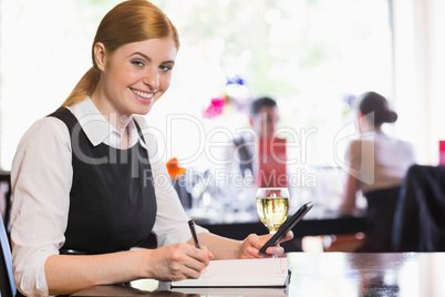 Smiling businesswoman holding phone and writing while looking at