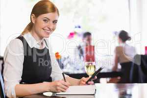 Smiling businesswoman holding phone and writing while looking at