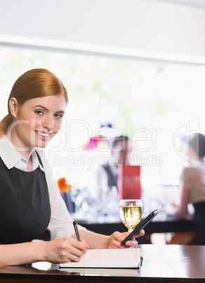 Smiling businesswoman writing and holding phone while looking at