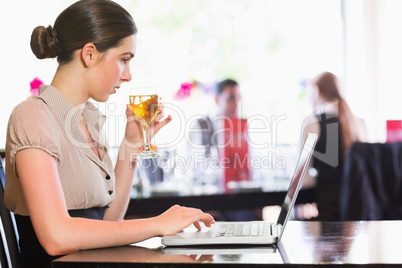 Attractive businesswoman holding wine glass while working on lap
