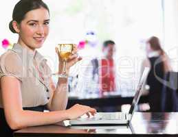 Happy businesswoman holding wine glass using laptop and looking