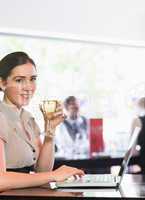 Smiling businesswoman using laptop while holding wine glass