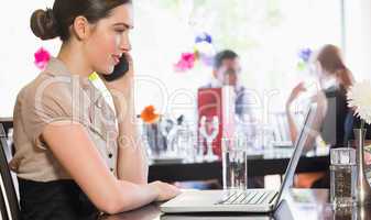 Businesswoman calling on phone while looking at laptop screen