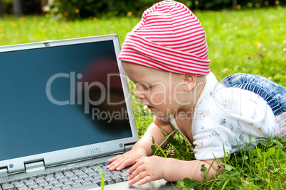 Small baby with laptop on the meadow