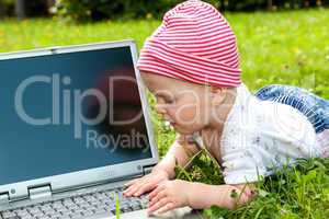Small baby with laptop on the meadow