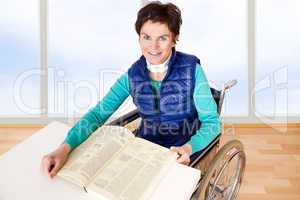 Woman with book sitting in a wheelchair at the table