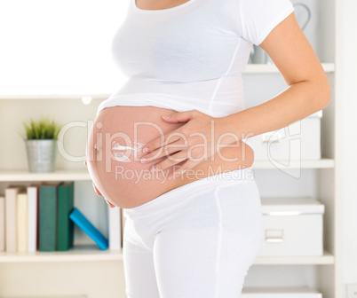 Pregnant woman applying lotion cream