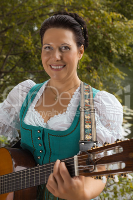 lächelnde bayerische frau im dirndl beim gitarre spielen am see
