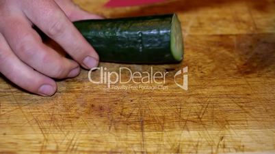 Cutting cucumber on wooden plate closeup