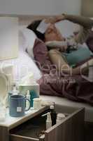 Flu medicines on bedside table ill woman