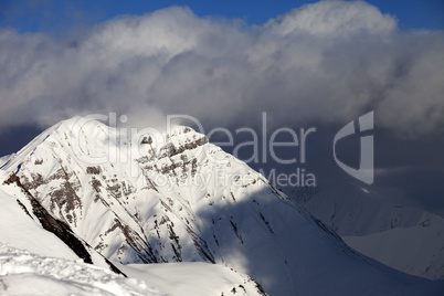 snowy sunlit mountains and blue sky with clouds