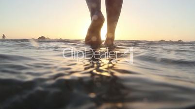 Beautiful female legs in the surf at sunset.