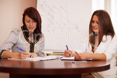 two women taking notes at a business presentation