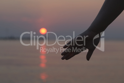 womans hand silhouetted against a sunset