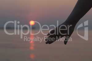 womans hand silhouetted against a sunset