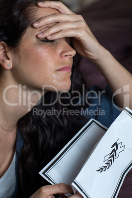 Crying young woman holding obituary