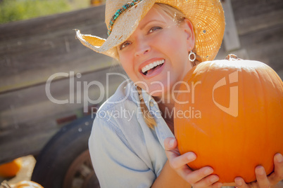 Beautiful Blond Female Rancher Wearing Cowboy Hat Holds a Pumpkin