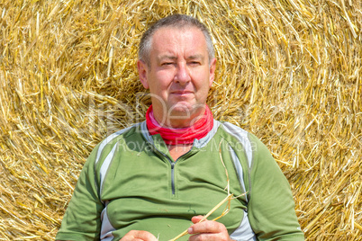 organic farmer sitting in front of bales of straw