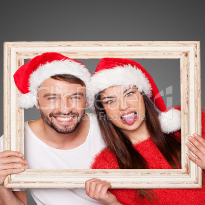 couple looking through frame wearing santa hats
