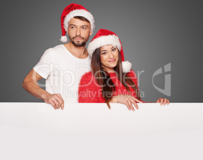 couple wearing santa hats holding a blank board