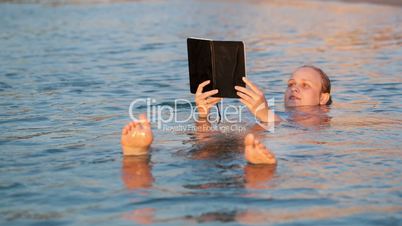 Woman smiling as she reads a book while swimming