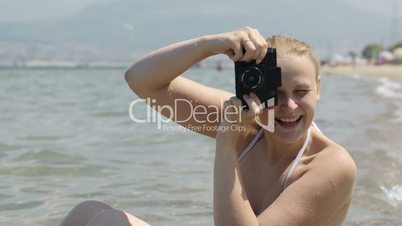 Smiling woman taking a photo at the seaside with her vintage camera