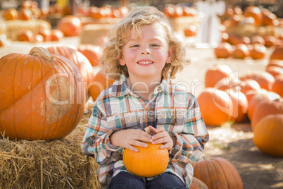 little boy sitting and holding his pumpkin at pumpkin patch.