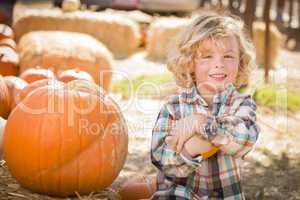 little boy sitting and holding his pumpkin at pumpkin patch.