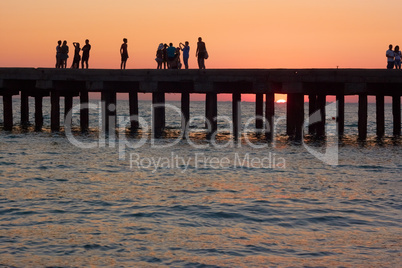 people on the old sea pier at sunset