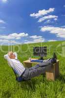 businessman relaxing feet up desk in green field