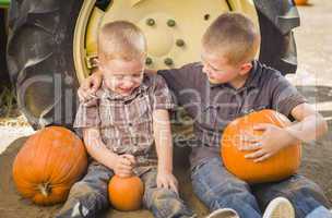 two boys holding pumpkins talking and sitting against tractor ti