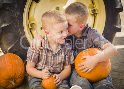 two boys sitting against tractor tire holding pumpkins whisperin