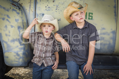 two young boys wearing cowboy hats leaning against antique truck