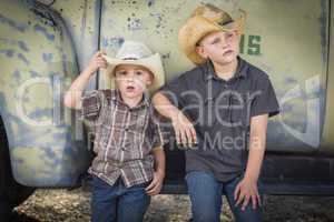 two young boys wearing cowboy hats leaning against antique truck