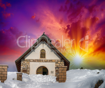 Chapel surrounded by snow on a mountan peak. Beautiful sunset co