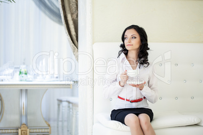 Young curly brunette drinking coffee in hotel room