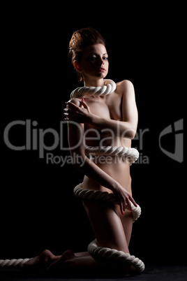 Slim naked girl wrapped by rope posing in studio