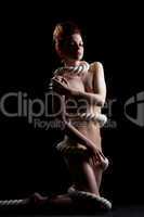 Slim naked girl wrapped by rope posing in studio