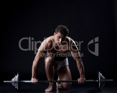 Sexual muscular guy posing with barbell in studio