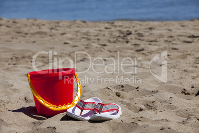 Flip Flops und ein roter Eimer am Strand
